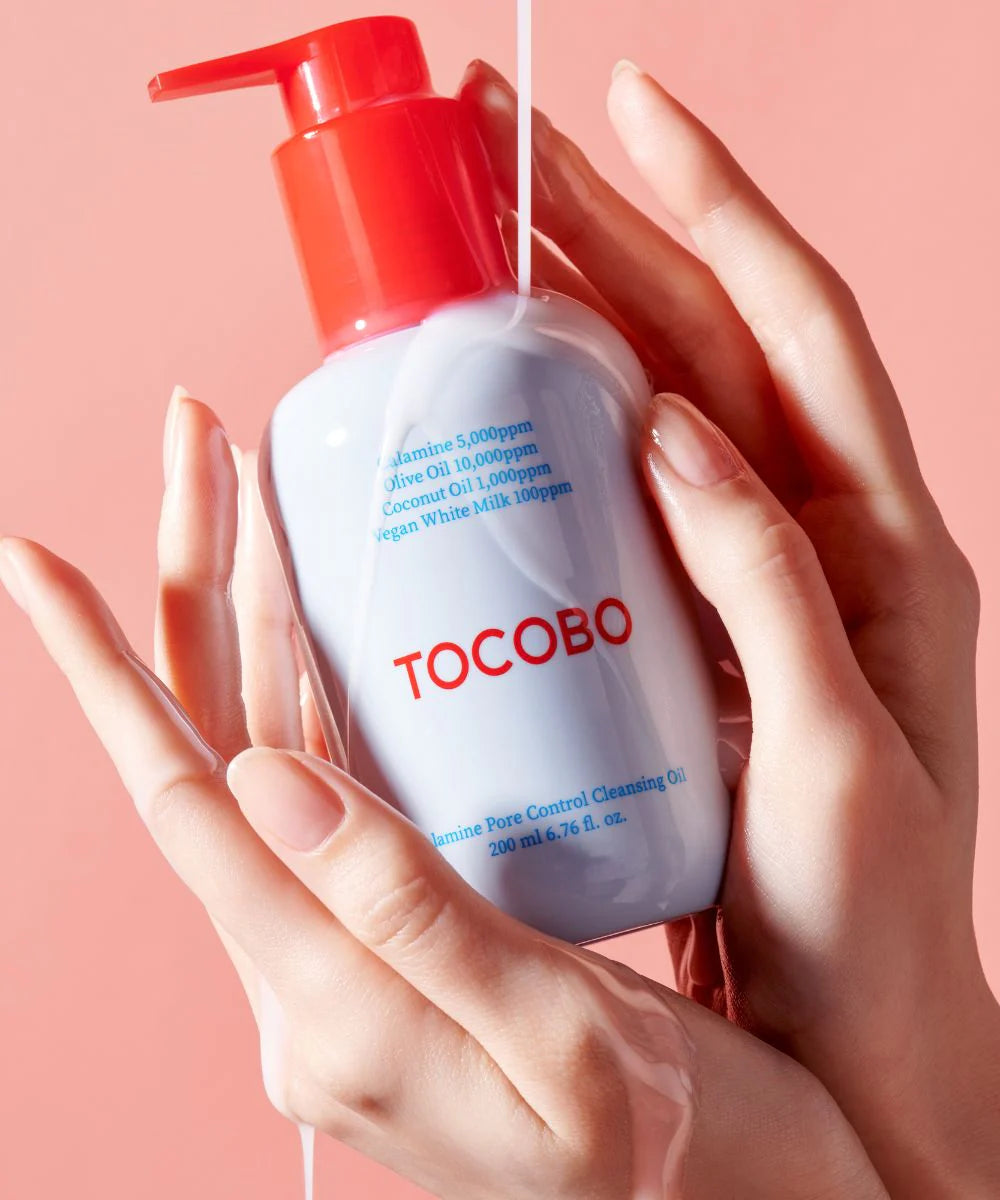 Hand holding a Tocobo skincare product against a pink background